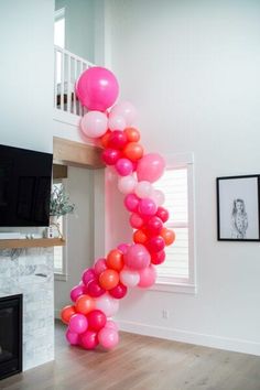 a bunch of pink and orange balloons hanging from the ceiling in a room with white walls