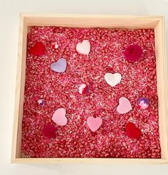 a wooden box filled with lots of hearts on top of pink sprinkles