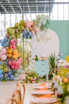 a room filled with lots of balloons and flowers on the wall next to a table