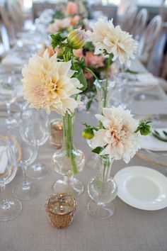 there are many flowers in vases sitting on the table with wine glasses and place settings