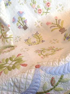 a quilted bed spread with flowers and leaves in pastel blue, green, pink and white colors