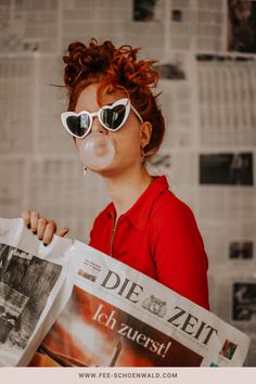 a woman wearing sunglasses and blowing bubbles while holding a newspaper in front of her face