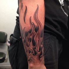 a man with a black and grey fire tattoo on his arm