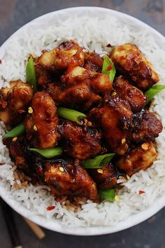 a white bowl filled with chicken and rice on top of a wooden table next to chopsticks