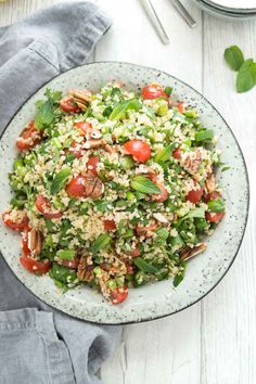 a salad with tomatoes, lettuce and pecans in a bowl on a white table