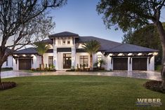 a large white house with two garages and trees in the front yard at dusk