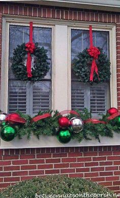 two christmas wreaths are hanging on the window sill in front of a brick building