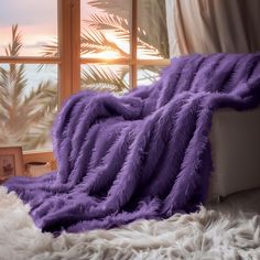 a purple blanket sitting on top of a bed next to a window