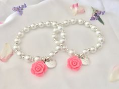 two bracelets with pink roses and pearls on white fabric next to flowery petals