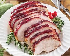 sliced pork with cranberry sauce and herbs on a white plate next to tomatoes