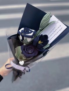 a bouquet of crocheted flowers is being held by someone's hand on the street