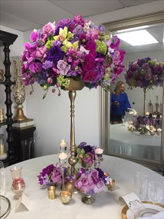 purple and green flowers in a gold vase on a white table cloth with candles around it