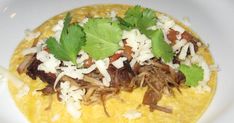 a taco topped with meat and cilantro on top of a white plate