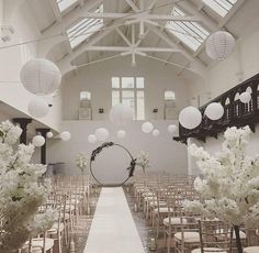 an indoor wedding venue with white flowers and lanterns hanging from the ceiling, along with rows of chairs