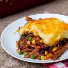 a white plate topped with meat and veggies covered in cheese on top of a table