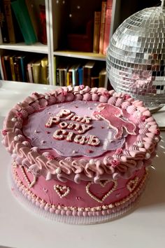 a pink cake sitting on top of a table next to a disco ball and bookshelf