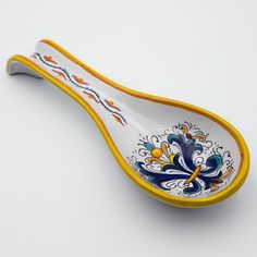 a yellow and blue spoon with designs on the side sitting on a white table top