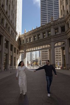 two people holding hands while walking through an open area in the middle of a city