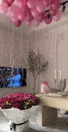 balloons are hanging from the ceiling in front of a table with flowers and a cake