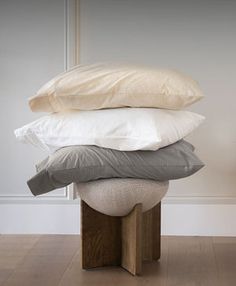 a stack of pillows sitting on top of a wooden stool in front of a white wall