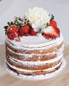 a cake with powdered sugar, strawberries and flowers on top is sitting on a table