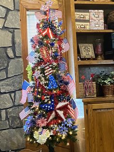 a decorated christmas tree with red, white and blue ribbons on it in front of a stone fireplace