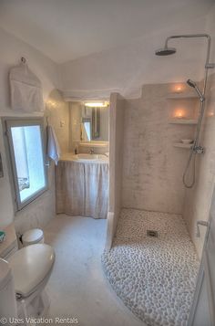 a bathroom with a walk in shower next to a white toilet and sink under a window