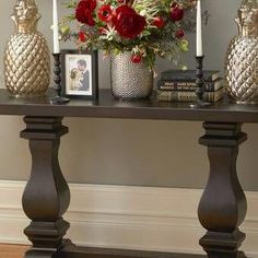 a table topped with vases filled with red flowers and greenery next to two candles