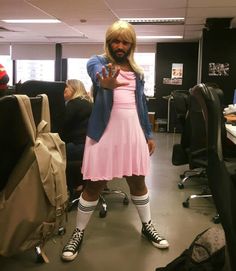 a man in a pink dress and white socks posing for the camera with his hand up