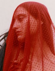 a woman with long hair wearing a red veil over her head and looking off to the side