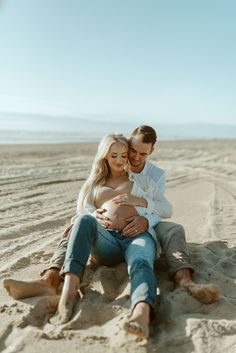 a pregnant couple sitting on the beach together