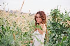 a beautiful young woman standing in the middle of a field with lots of tall grass