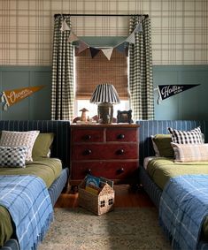 two twin beds in a bedroom with blue and green bedding, striped curtains and pillows