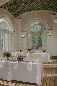 the table is set with white linens and pink flower centerpieces on it