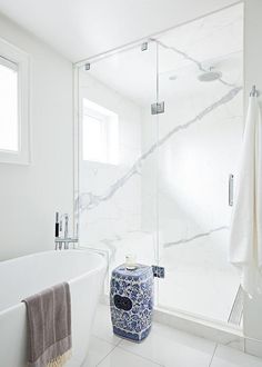 a white bathroom with a blue and white vase next to the bathtub in it