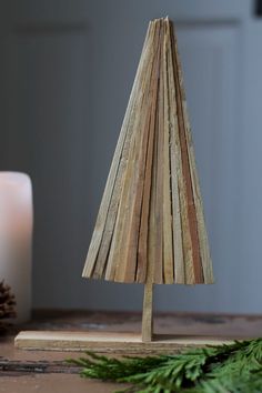 a small wooden christmas tree on a table next to two white candles and pine cones