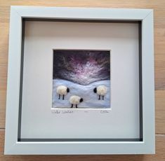 three sheep are standing in the snow under a pink and purple sky, framed in a white frame