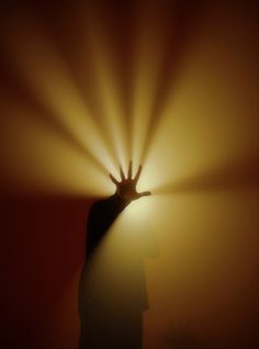 a person holding their hand up in the air with light coming through it and behind them