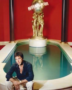 a man sitting in front of a fountain with a golden statue behind him on top of it