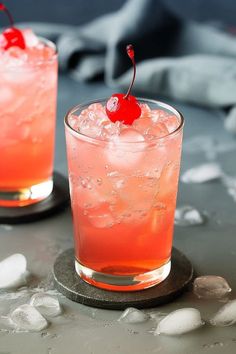 two glasses filled with pink liquid and topped with a cherry garnish, sitting on a table