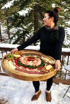 a woman is holding a platter with food on it in the snow near some trees