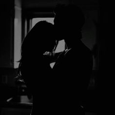 black and white photograph of a man kissing a woman's head in the dark