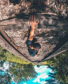 a man standing on top of a wooden bridge next to trees and water with his hands in the air