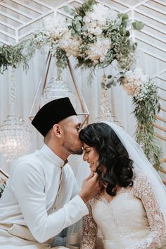 a bride and groom are sitting on the floor in front of a floral arch with greenery