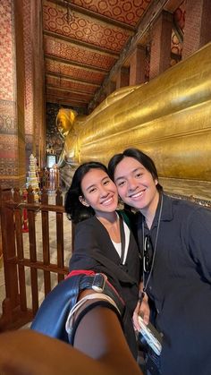 two women taking a selfie in front of a large golden reclining buddha statue