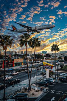 an airplane is flying over a busy city street with palm trees in the foreground