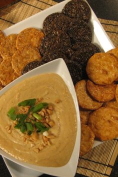 a white plate topped with crackers and dip next to other foods on a table