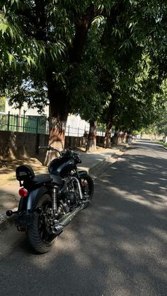 a black motorcycle parked on the side of a road next to a tree filled street