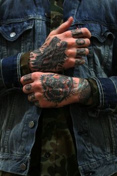 a man with tattoos on his arms and hands is wearing a denim jacket, camo pants