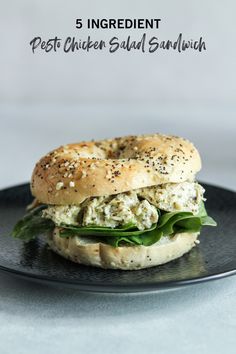 a bagel sandwich on a black plate with sesame seeds and chicken salad in the middle